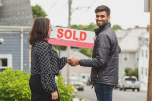 smiling homeowner shaking hands with sold sign in background