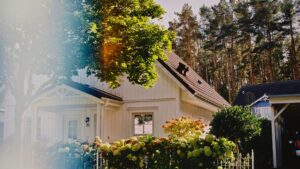 White cottage surrounded by vibrant garden and forest trees in Berlin, showcasing a serene summer setting.
