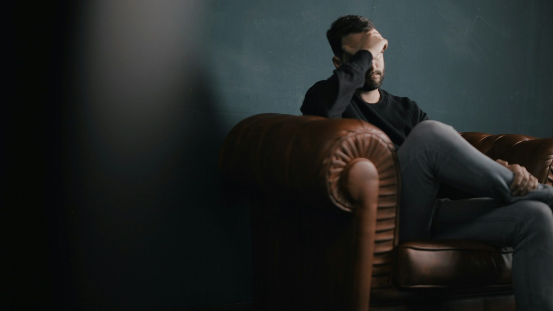 Sad man sitting on a couch covering his face