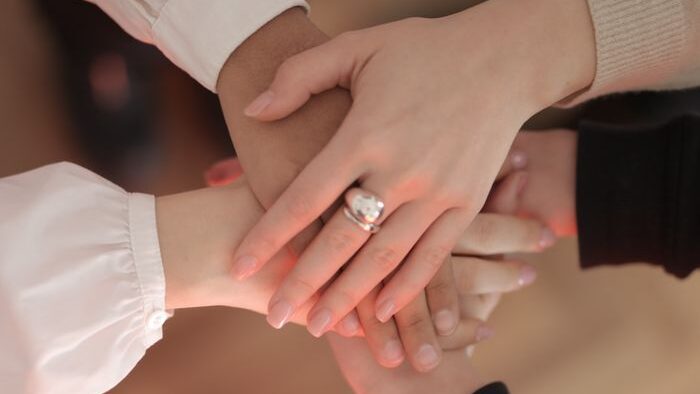 Top view of faceless friends in different clothes stacking hands together while standing on wooden floor indoor on sunny day