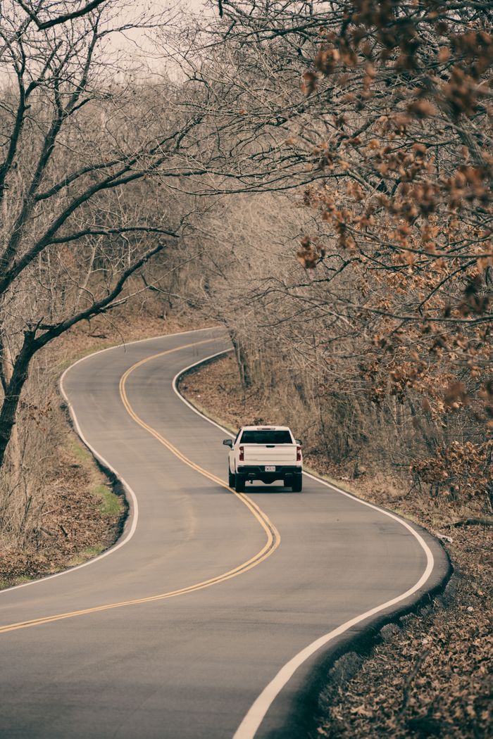 A lone vehicle travels a winding road amidst bare trees, showcasing the tranquil beauty of a Missouri landscape in winter.